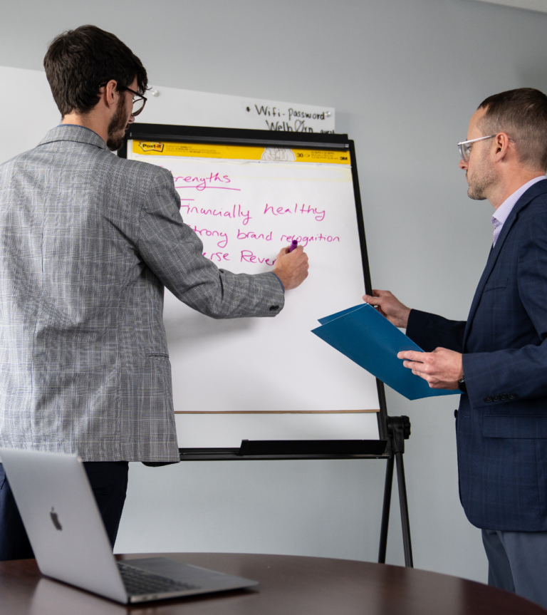 Services - Two business professionals collaborate on a company strategy, writing ideas on a flip chart during a planning meeting.
